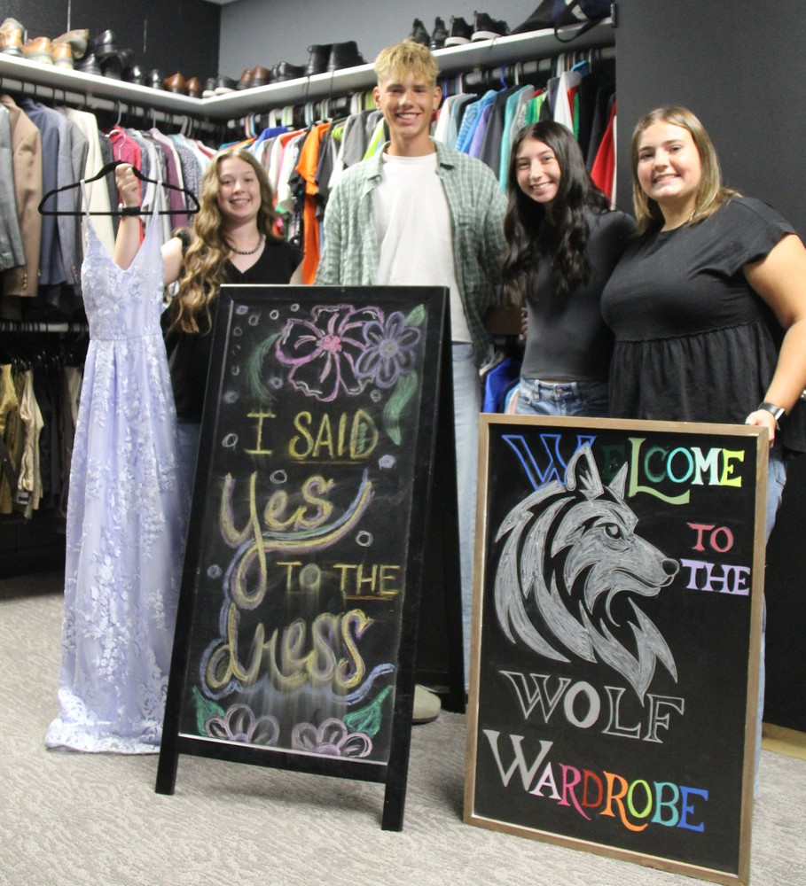 four students standing behind signs for the school's clothes closet