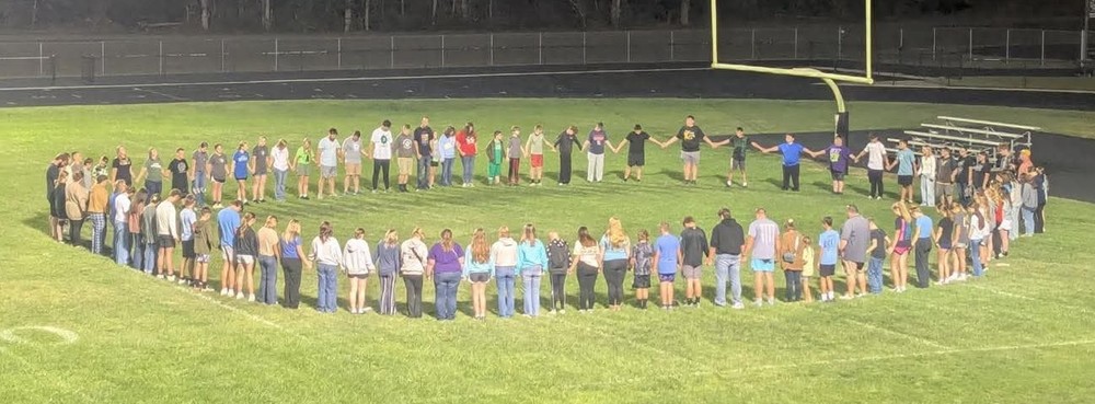 students standing in a circle holding hands for a time of reflection
