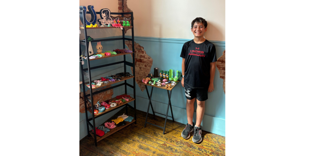 photo of a boy standing next to his 3-D creations that are placed on shelves