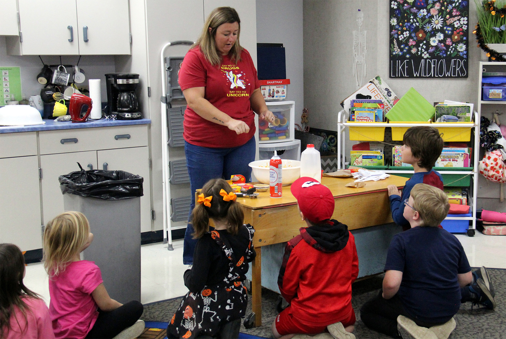 a teacher showing students how to make mini pumpkin pies
