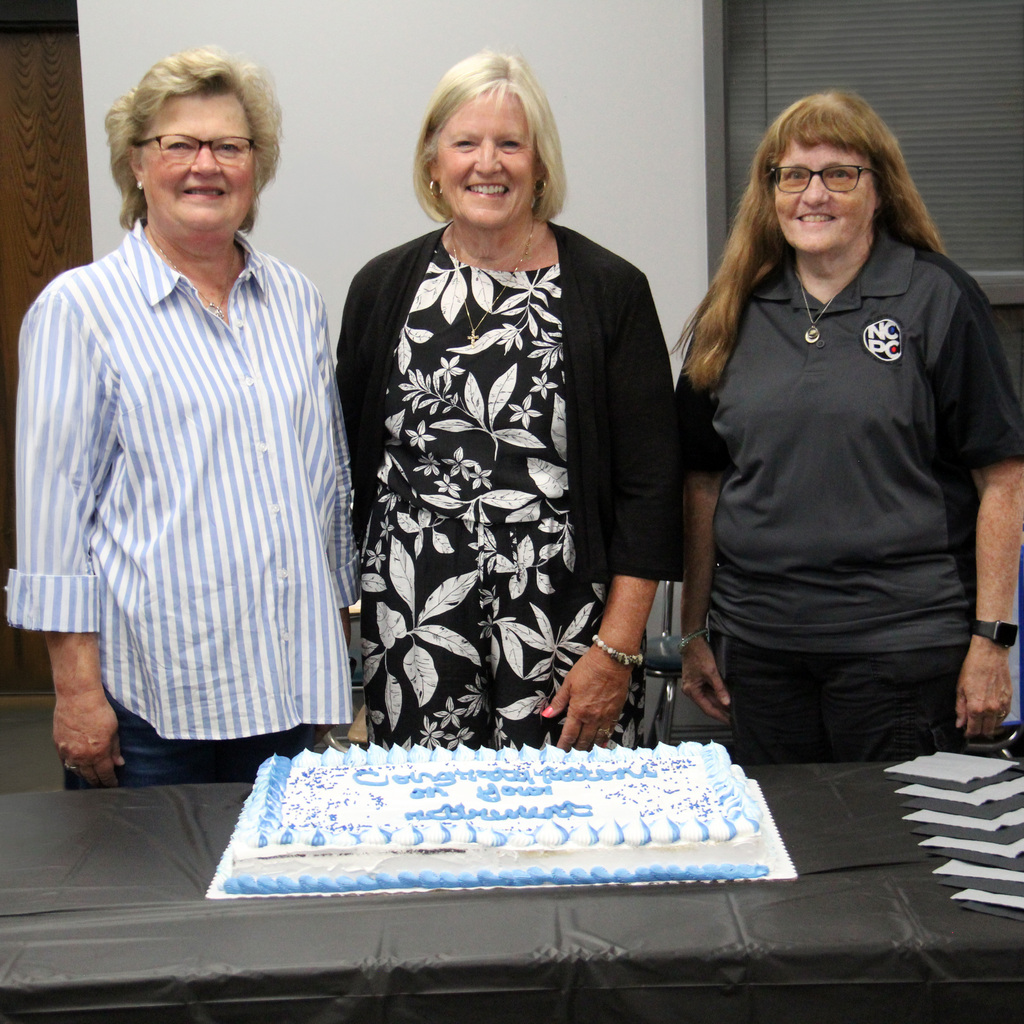 Left to Right: Mary Wicker, Jane McMullen, and Lori Brown pictured in front of a cake with congratulations on your retirement.