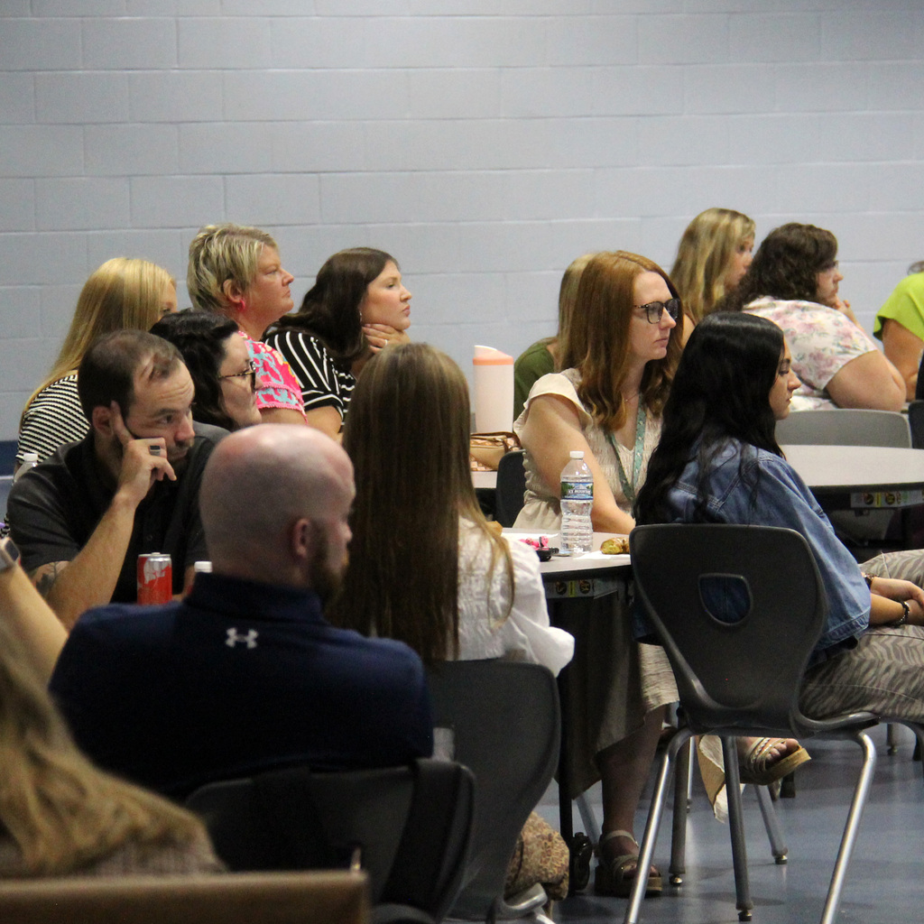 Staff members listen to a presentation during a school-wide meeting in the cafeteria.