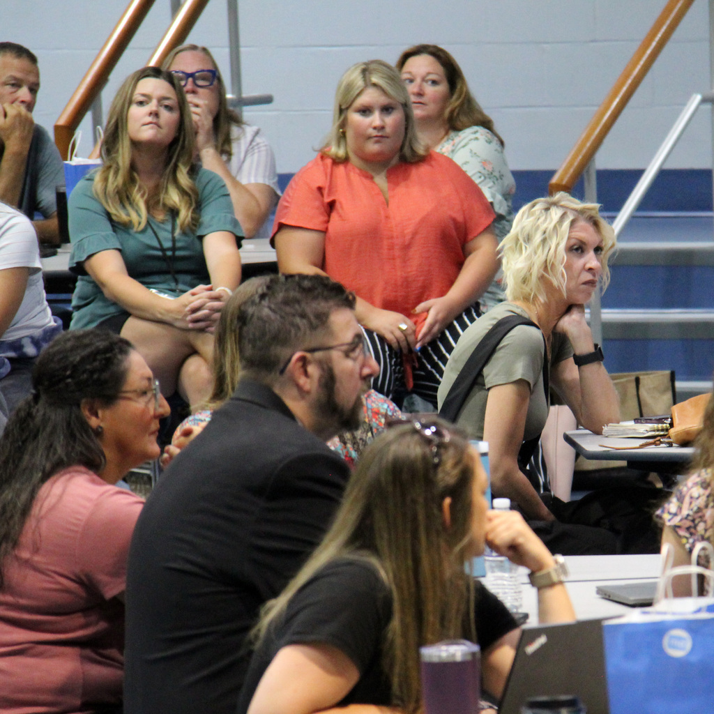 Staff members listen to a presentation during a school-wide meeting in the cafeteria.