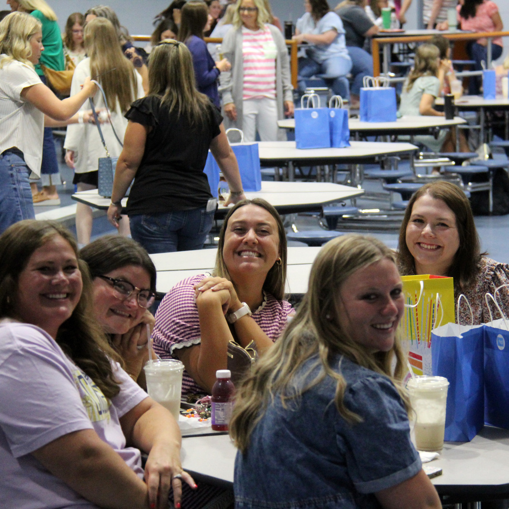 School staff smile for the camera while gathered at tables during a back-to-school staff meeting.