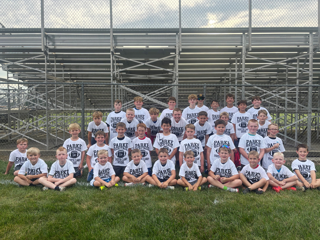 Group photo of youth football camp participants wearing matching Parke Heritage Youth Camp shirts, posing on the field in front of stadium bleachers.