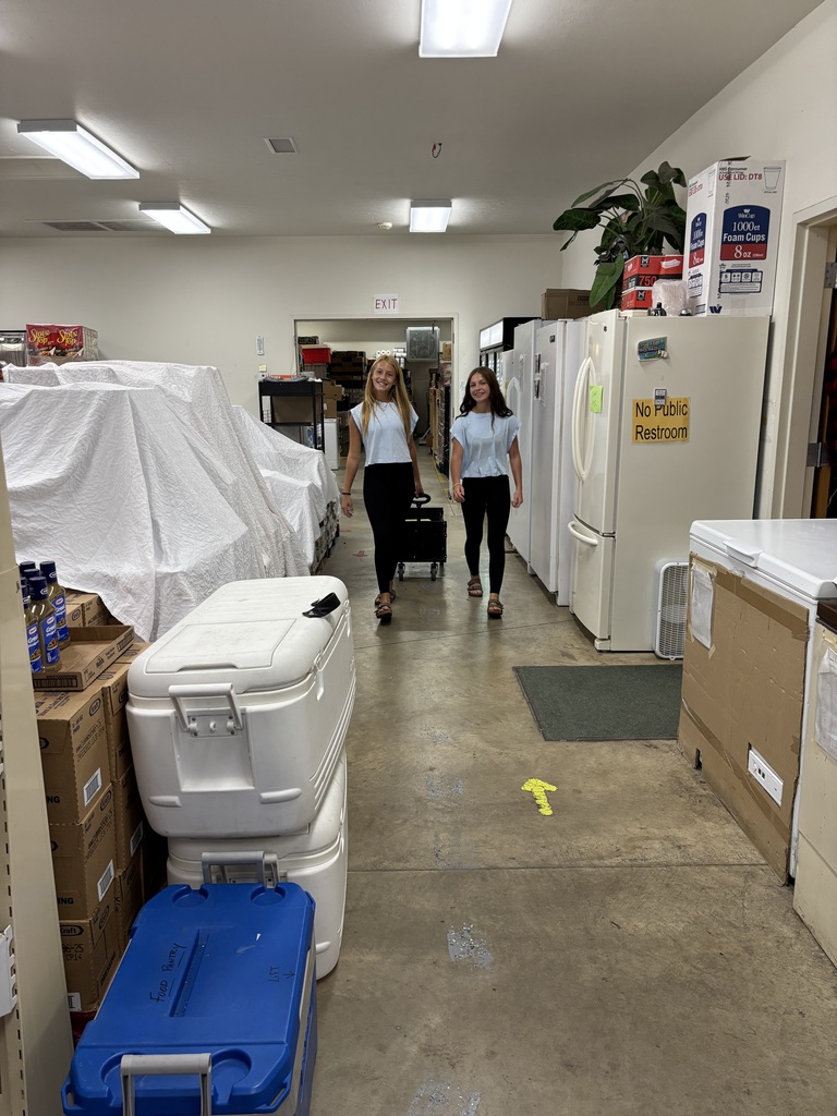Photo of two students, rolling a cart through the food pantry, to go stock shelves for volunteer hours. 