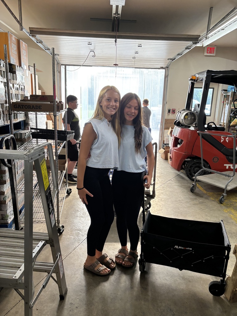 Photo of two students posing for a photo, getting ready to work, at the food pantry for volunteer hours. 