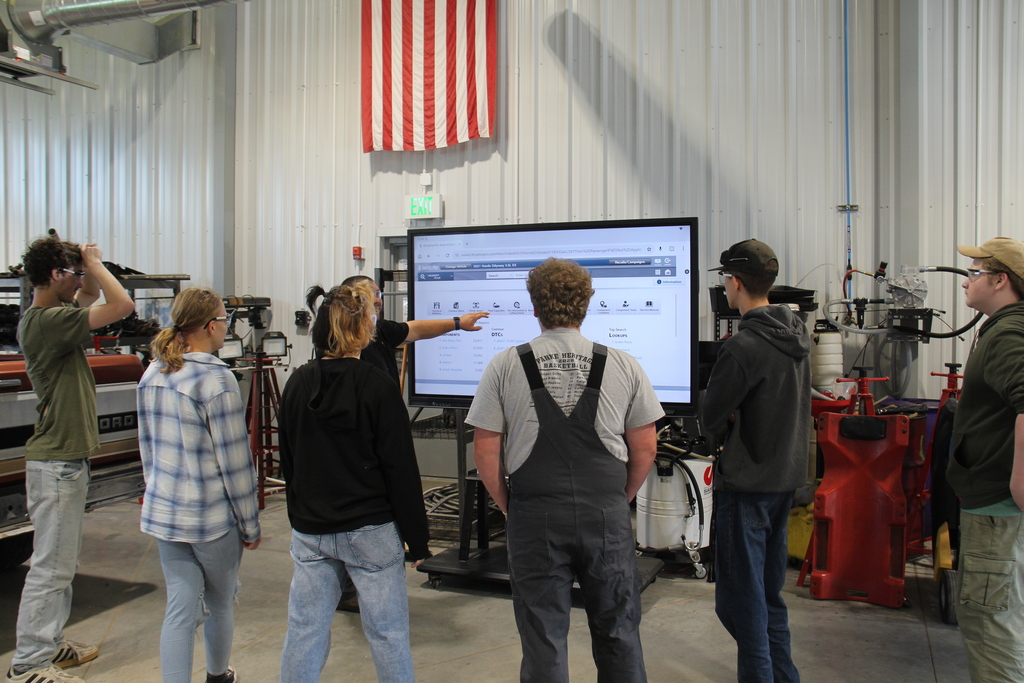 Auto Service students stand around the large monitor as auto service teacher shows them the schedule and what they will be doing. 