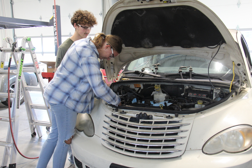 2 students lean inside the hood of a car to check it out. 