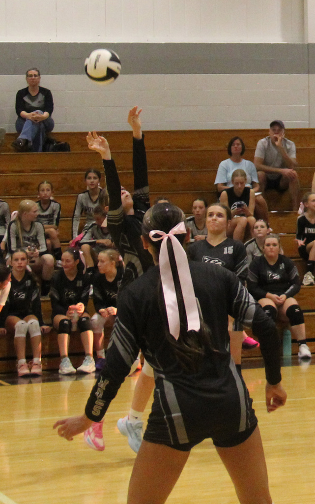 One player with her hands in the air to bump the ball and another girls back as she stands in anticipation.