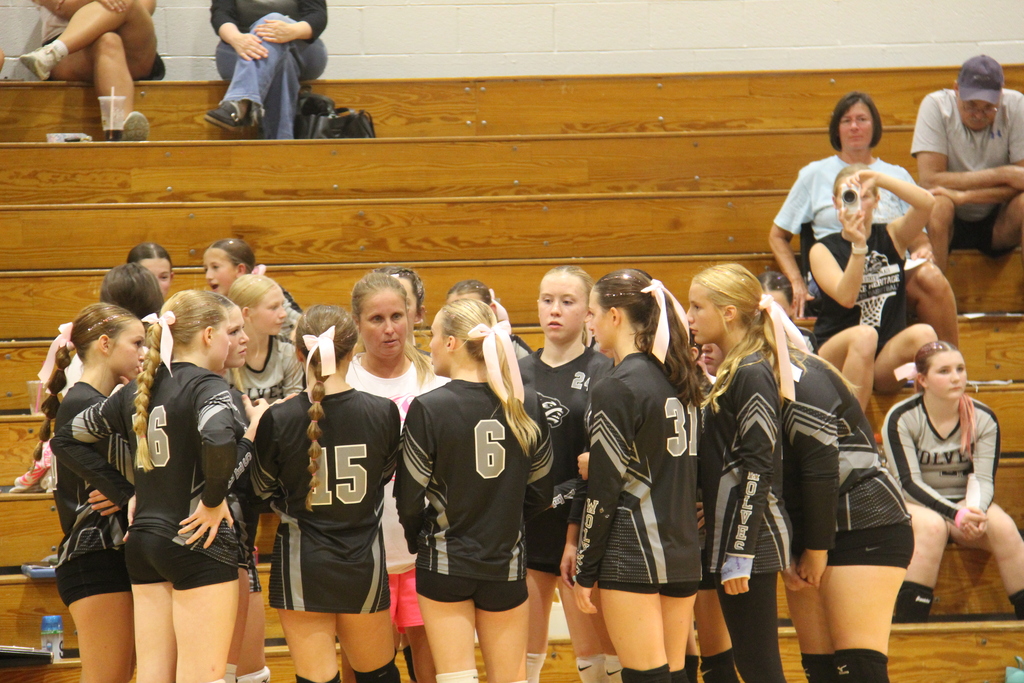 8th grade volleyball players stand in a circle during a time out while the coach talks to them. 