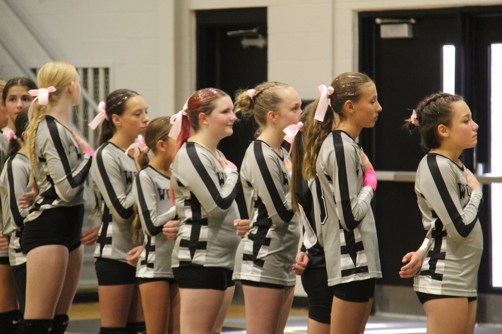 7th Grade Volleyball team stand with their hands on their chest for the national anthem.