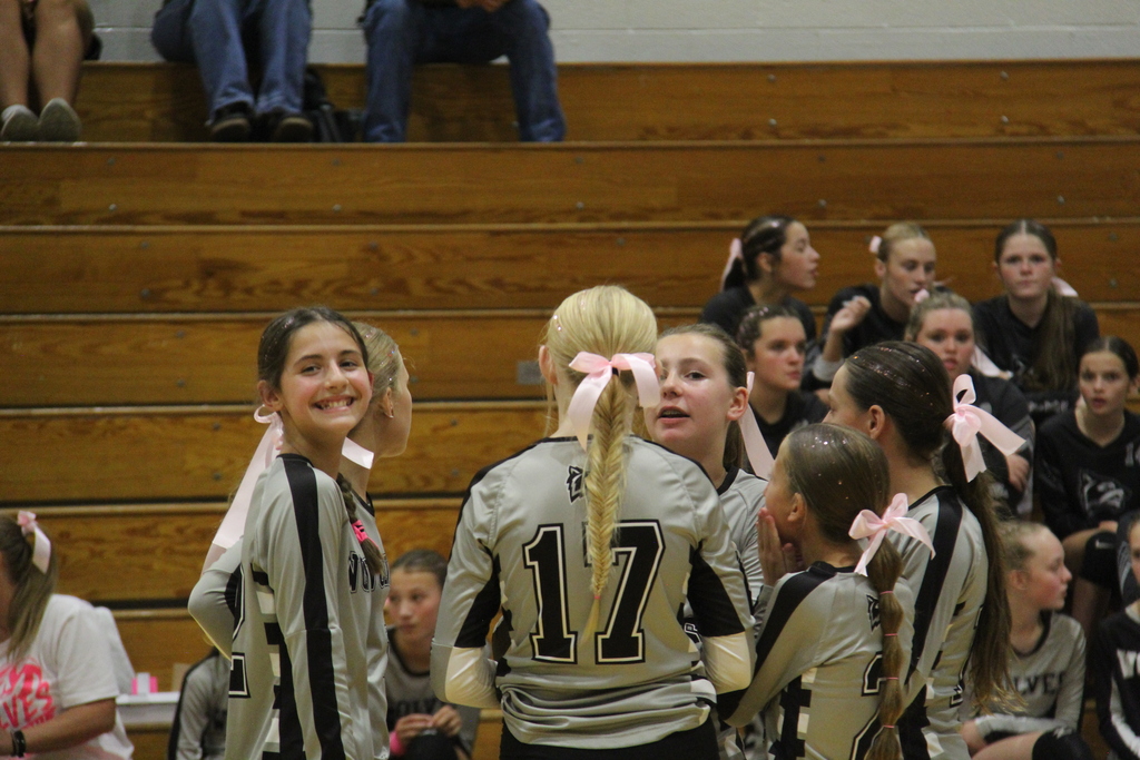 Volleyball team standing in a circle talking during a break. One girl is facing the camera with a big smile. 