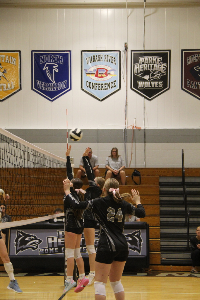 Two eighth graders jumping at the net to spike a ball. One player standing ready to also bump the ball.