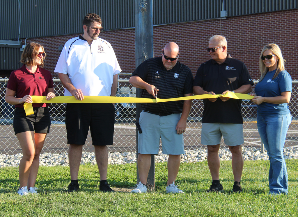 3 individuals from Riddell National Bank and the principal and the athletic director at the ribbon cutting ceremony. The athletic director is cutting the ribbon.