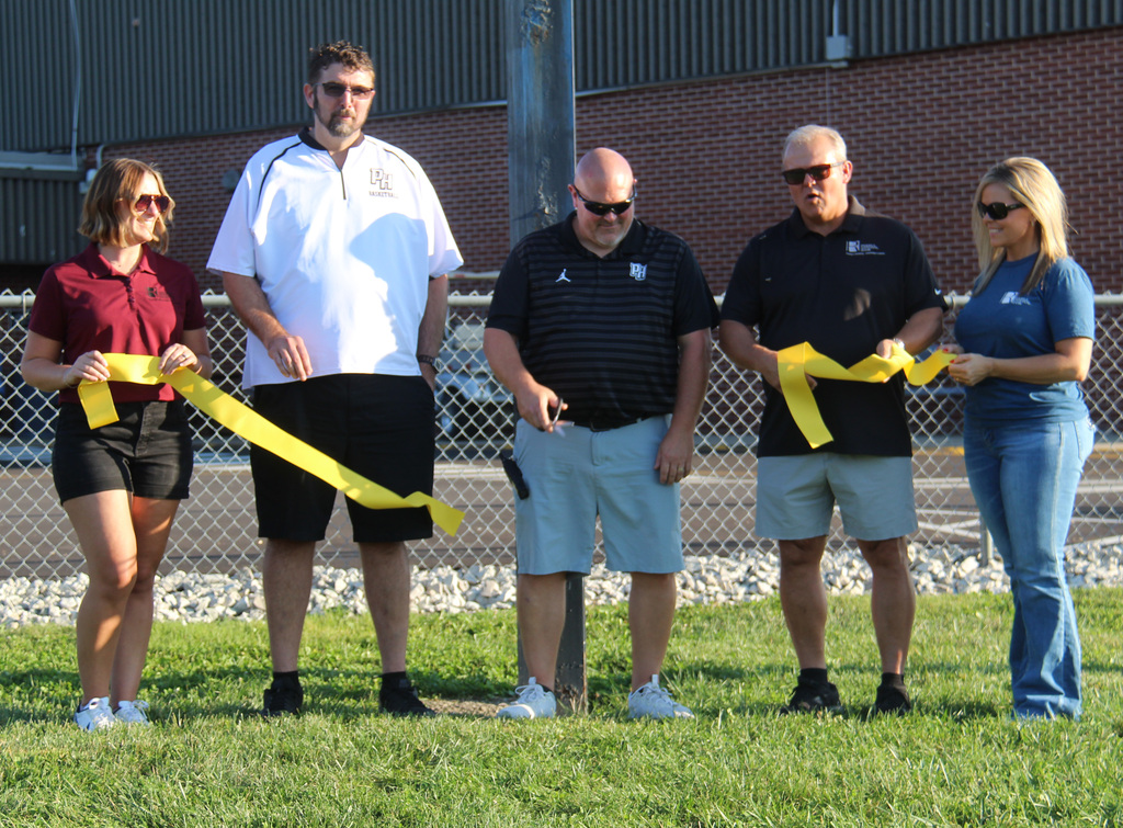 3 individuals from Riddell National Bank and the principal and the athletic director at the ribbon cutting ceremony. The athletic director is cutting the ribbon.