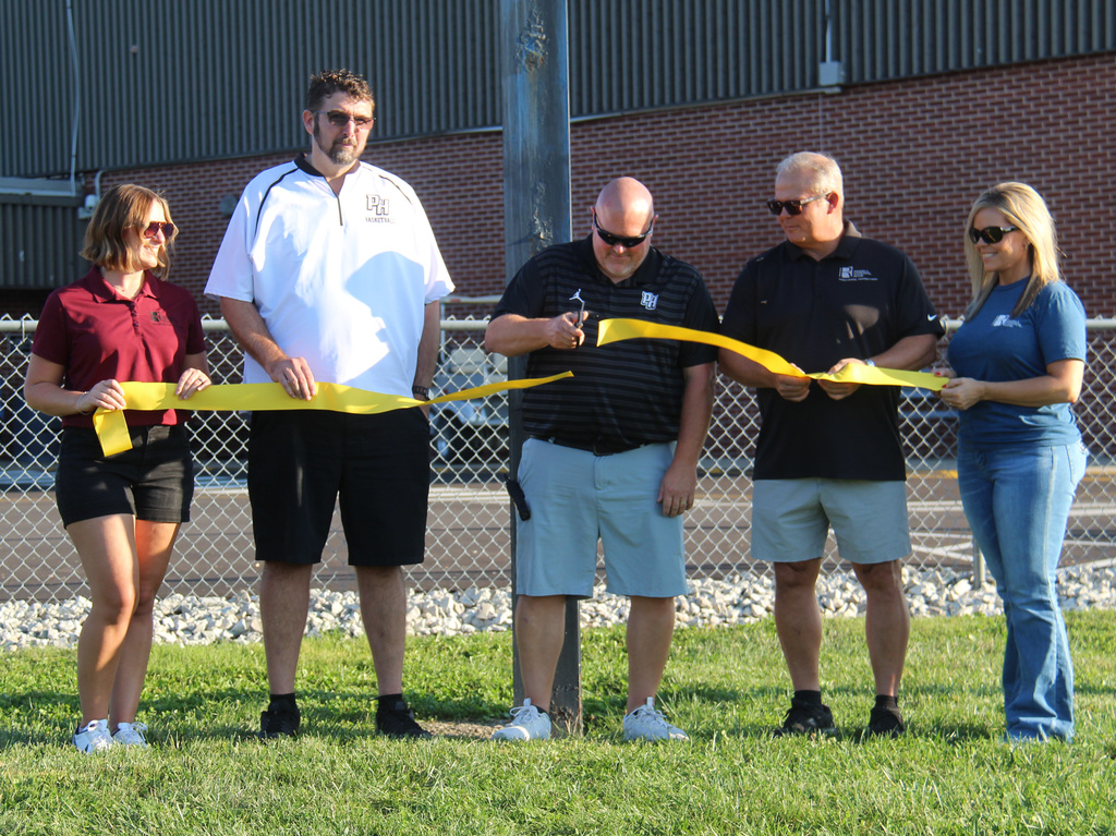 3 individuals from Riddell National Bank and the principal and the athletic director at the ribbon cutting ceremony. The athletic director is cutting the ribbon.