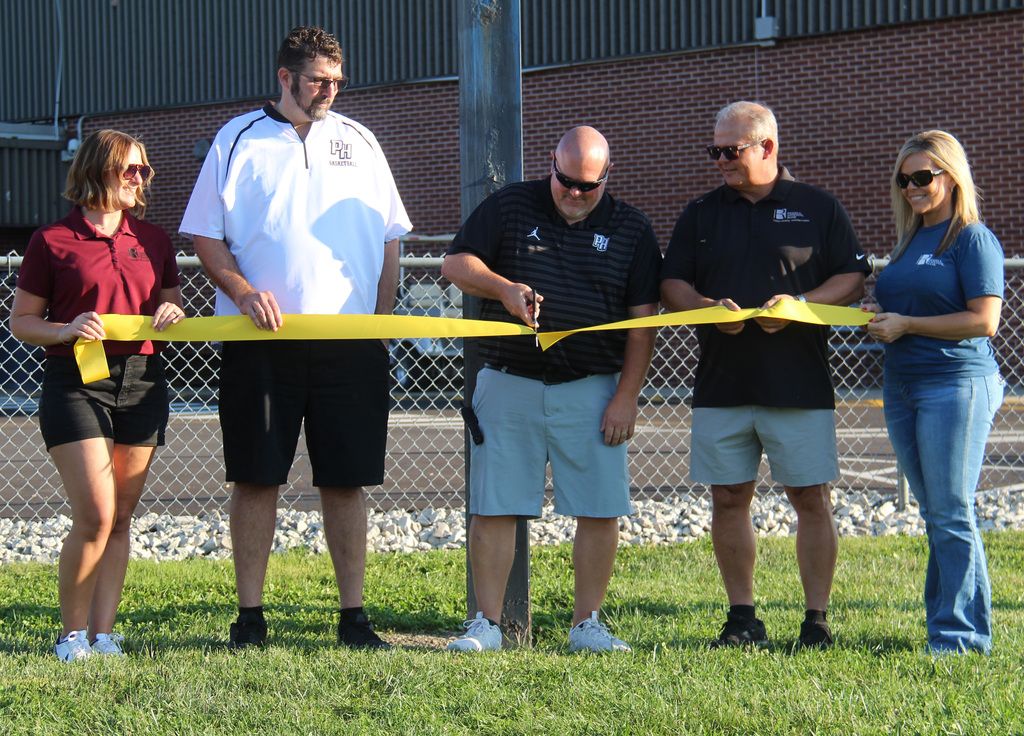 3 individuals from Riddell National Bank and the principal and the athletic director at the ribbon cutting ceremony. The athletic director is cutting the ribbon.