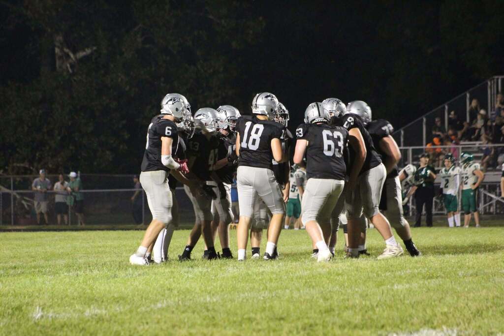 Parke Heritage football players in black jerseys and silver helmets gather together on the field during a nighttime game.