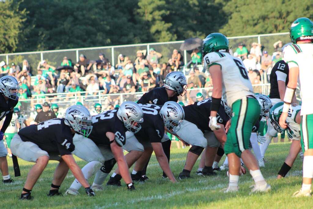 Parke Heritage football players line up at the line of scrimmage against an opposing team in green and white uniforms as spectators watch from the stands.