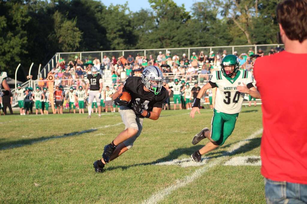 A Parke Heritage football player in a black uniform runs with the football while an opposing player in a green and white uniform pursues him.