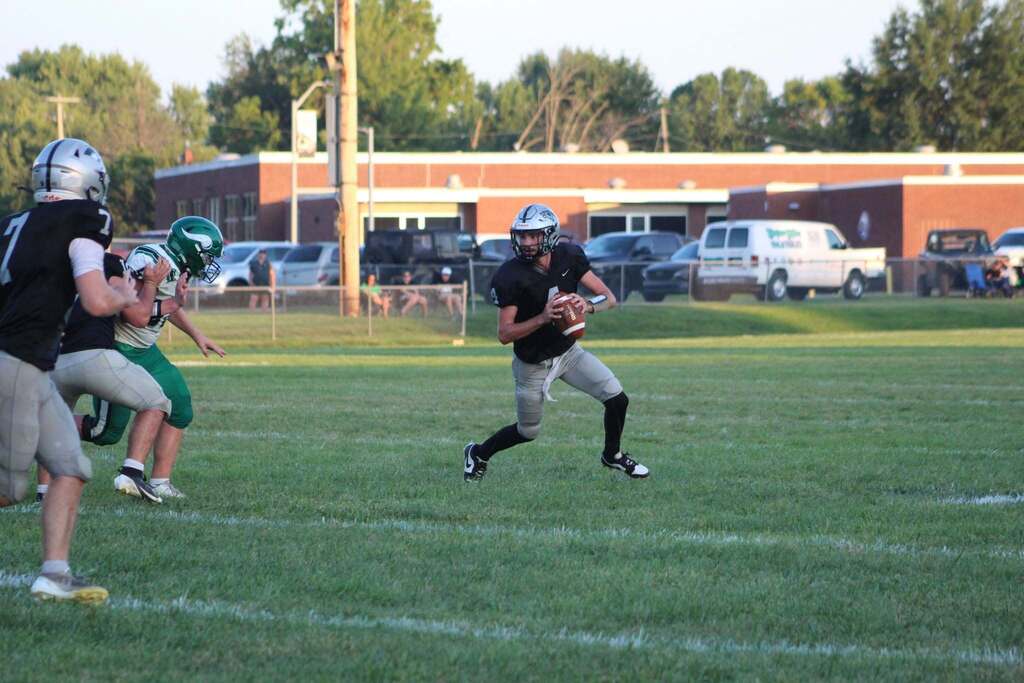 A Parke Heritage football player in a black jersey runs with the football while teammates block a defender in green and white uniforms.