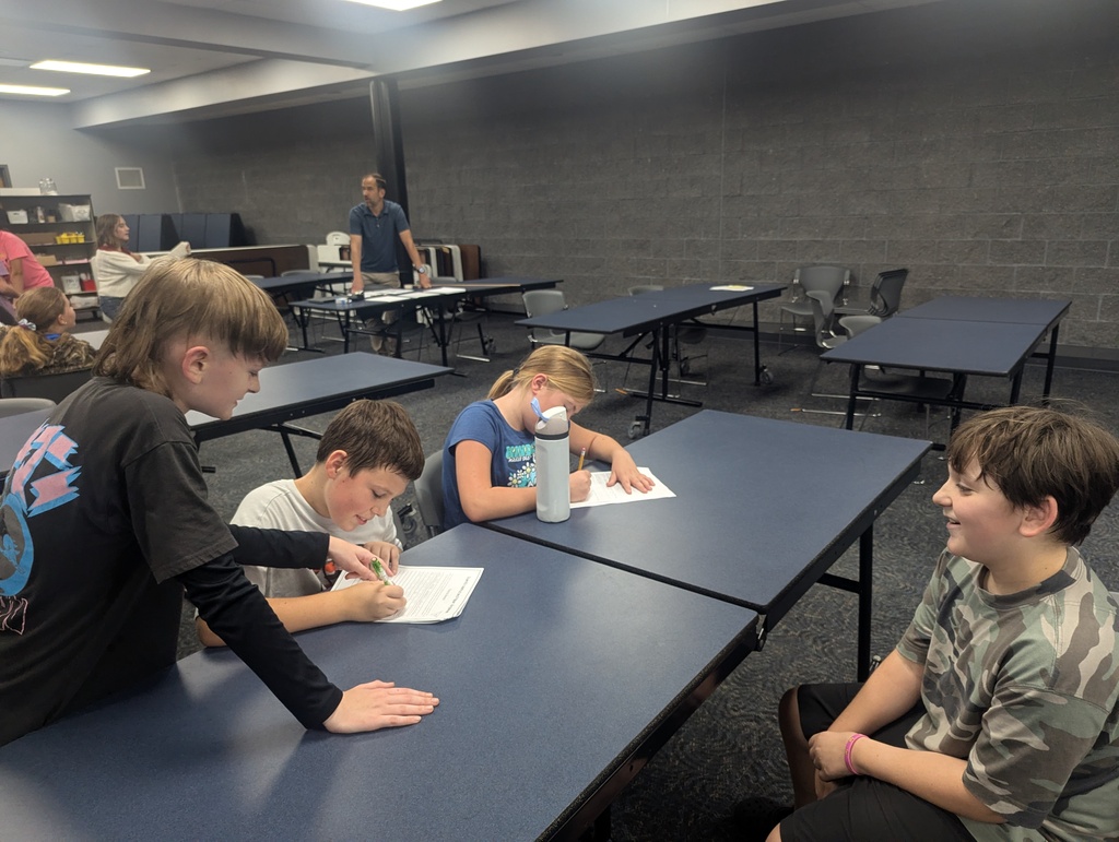 4 students sitting or standing around while working on their conclusion of findings while doing their hypothesis.