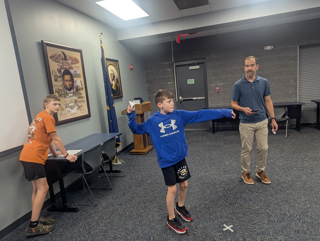 One student getting ready to fly his paper airplane while a student in his group and the teacher watch.