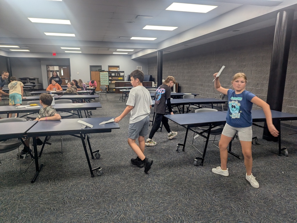 Several children flying their paper airplanes in the ELC. room.