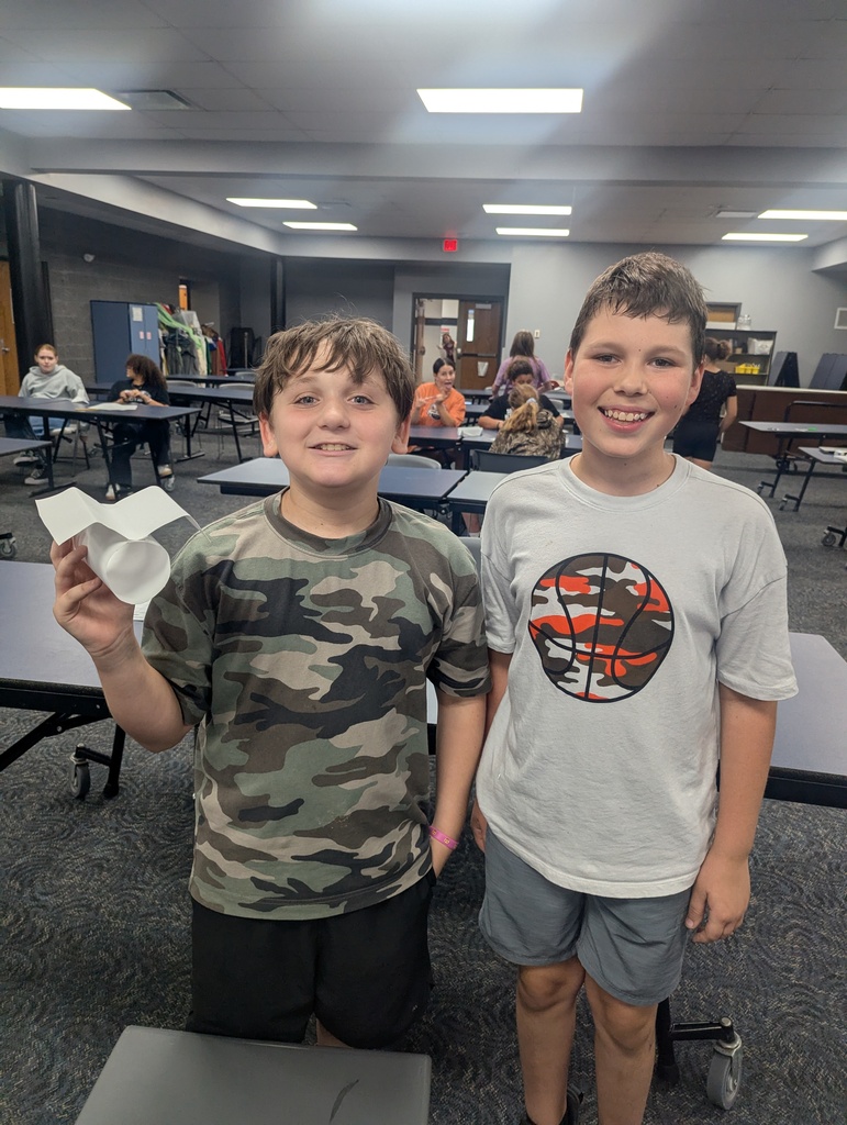 One student holding his paper airplane while him and another student pose for a photo.