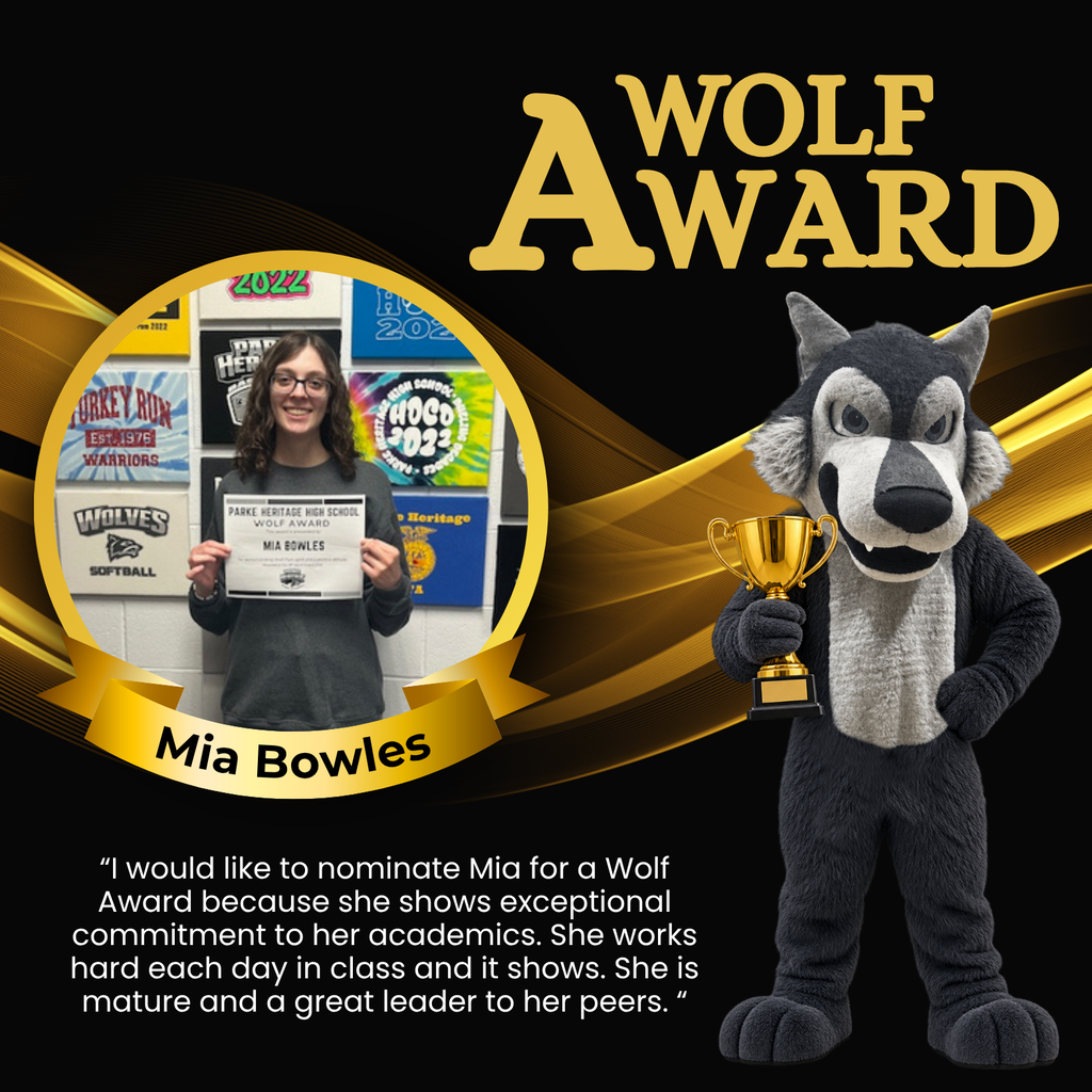 Photo of Mia wearing glasses and holding her Wolf Award certificate in front of a wall decorated with Parke Heritage and school activity signs.