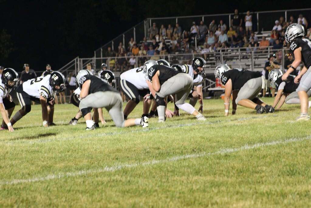Football teams line up at the line of scrimmage under the stadium lights.