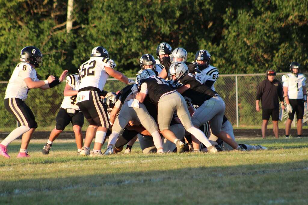 Players from both teams battle for possession in a crowded tackle on the field.