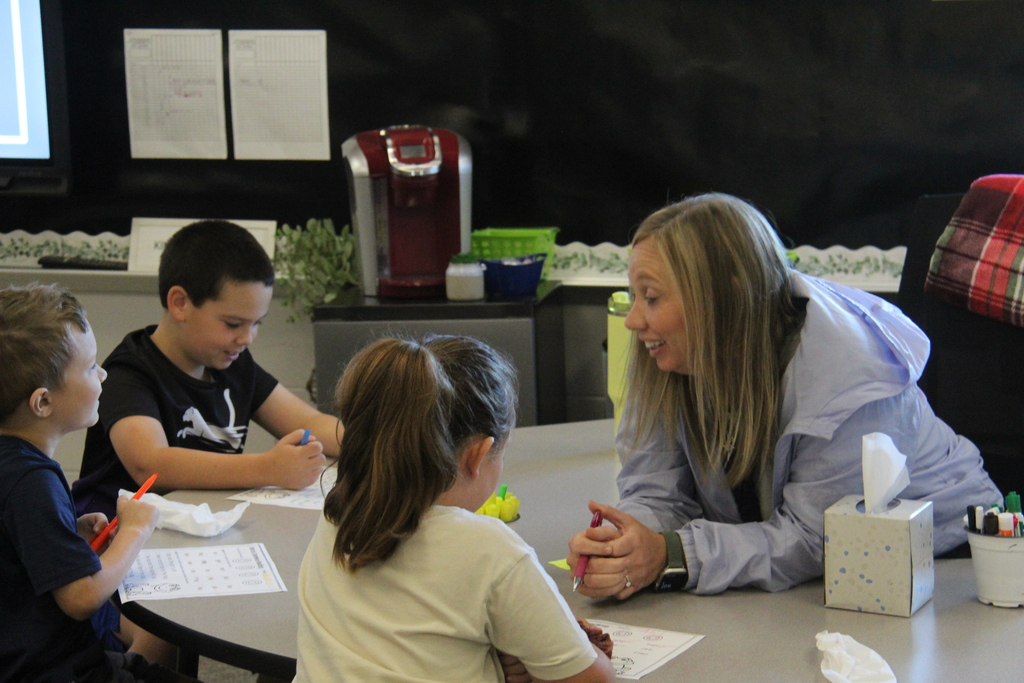 Teacher sitting at the table helping a few students sitting across from her. 