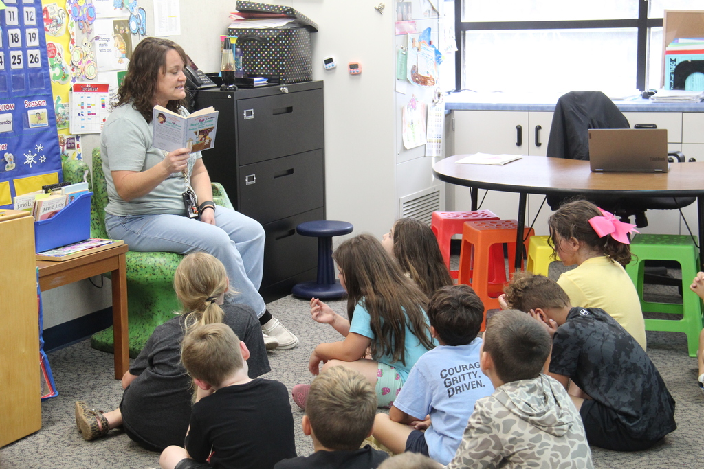 Teacher reading a book while her students sit on the floor around her. 