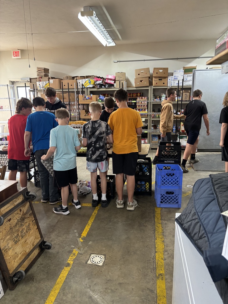 Students work as a team inside the food pantry, sorting and organizing food donations on tables and shelves.