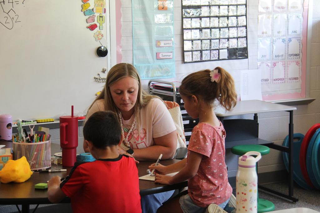 A group of second-grade students works on whiteboards while seated on the classroom floor during a lesson.