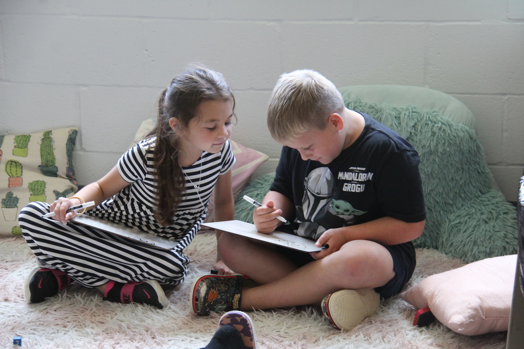 Two second-grade students sit together on a classroom rug, working on whiteboards and learning alongside one another.