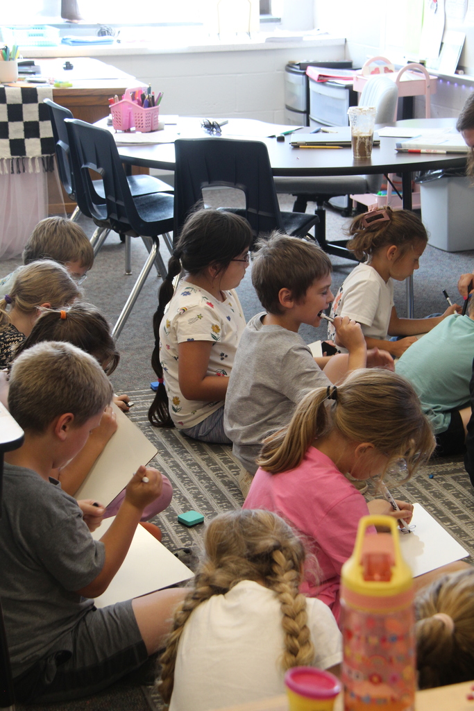 Second-grade students sit together and work on whiteboards while their teacher leads a math lesson displayed on an interactive board.
