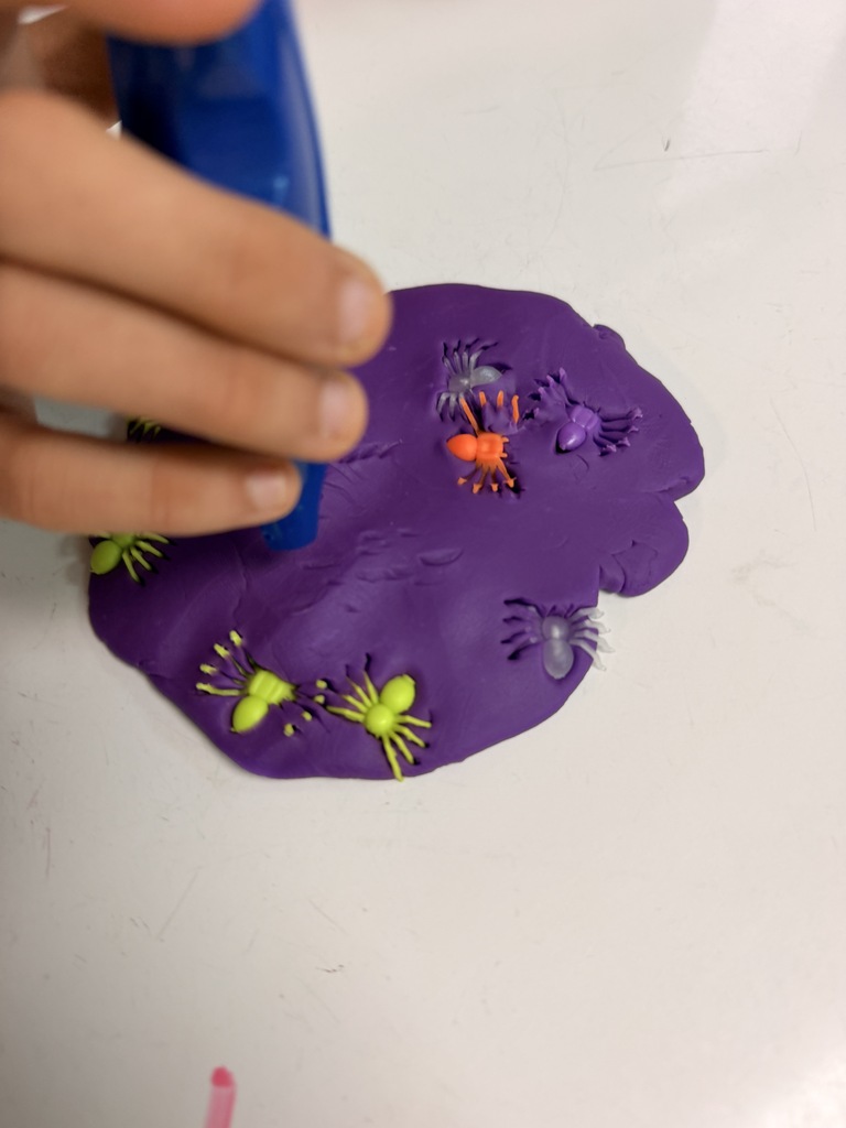 A childs hand pressing colored plastic spiders into purple playdoh. 