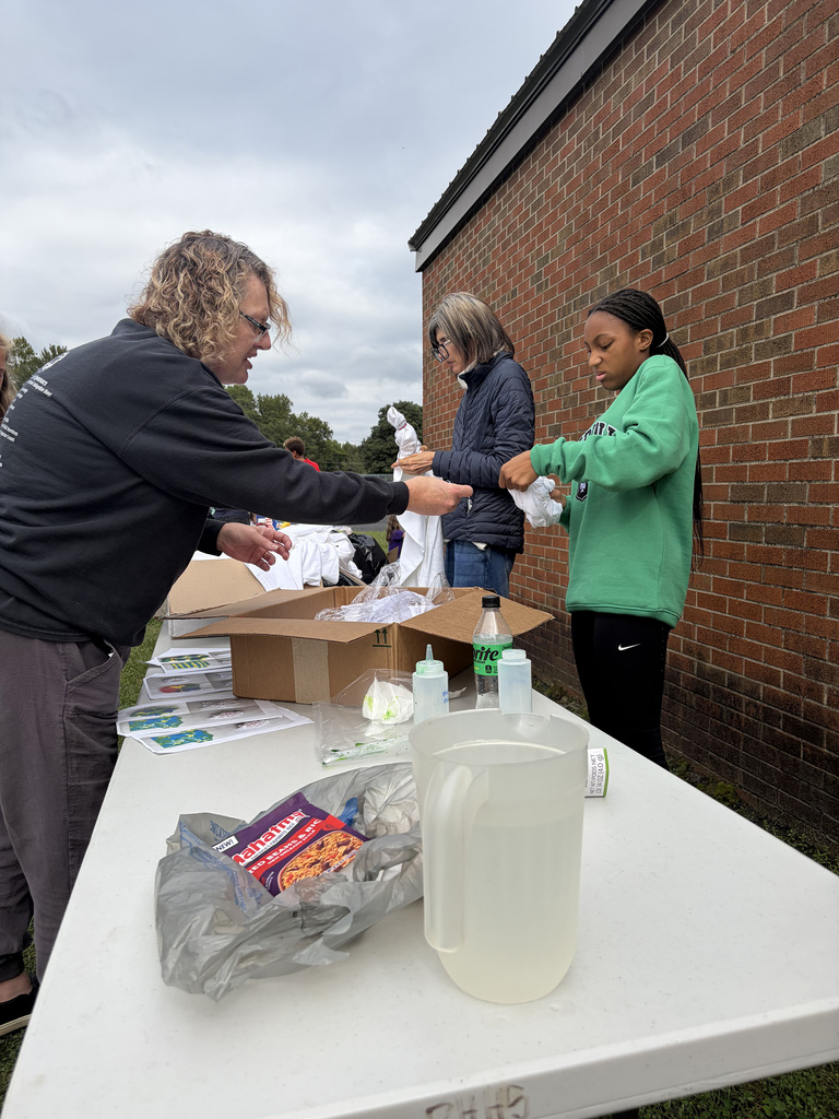 A parent and a student helping roll shirts to tie-dye at the Bindi BBQ.