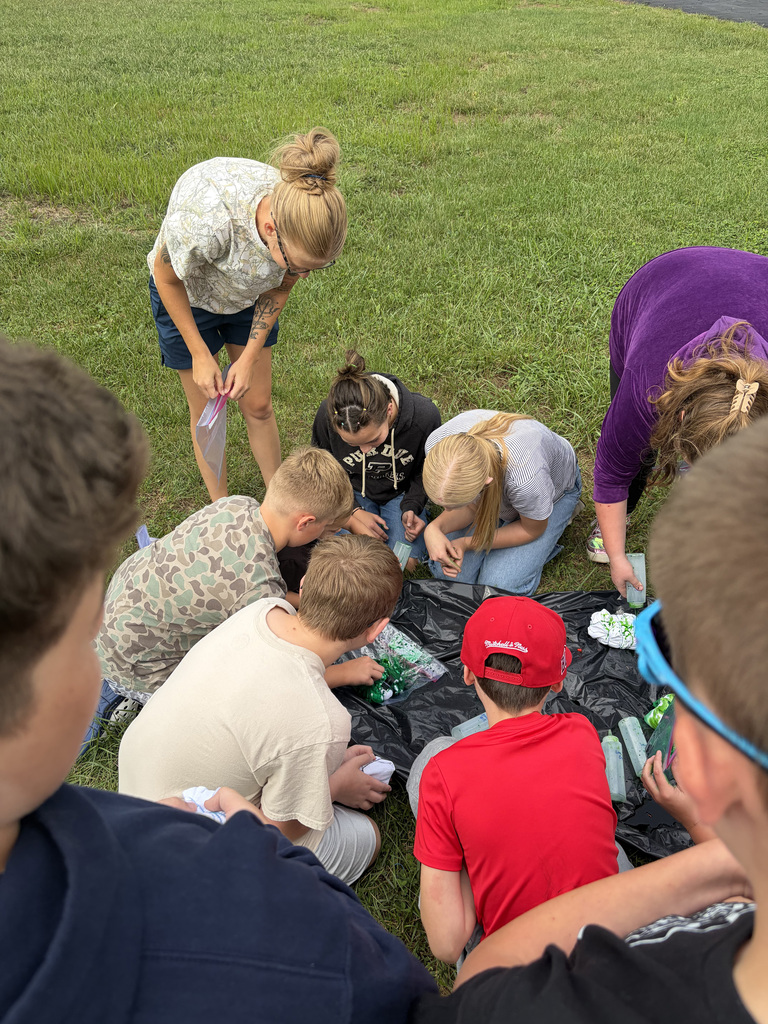 9 students standing and sitting in a circle tie-dying their shirts at the Bindi BBQ.