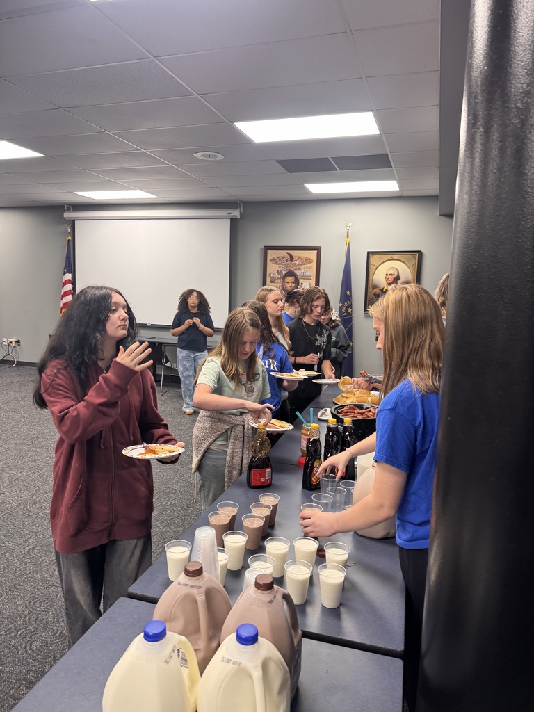 Students line up to get food while others stand behind the table to serve them. 