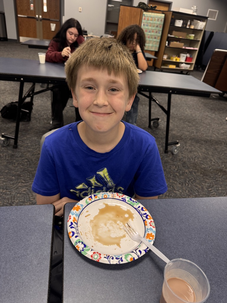 One student smiles for a photo with his empty pancake plate in front of him.