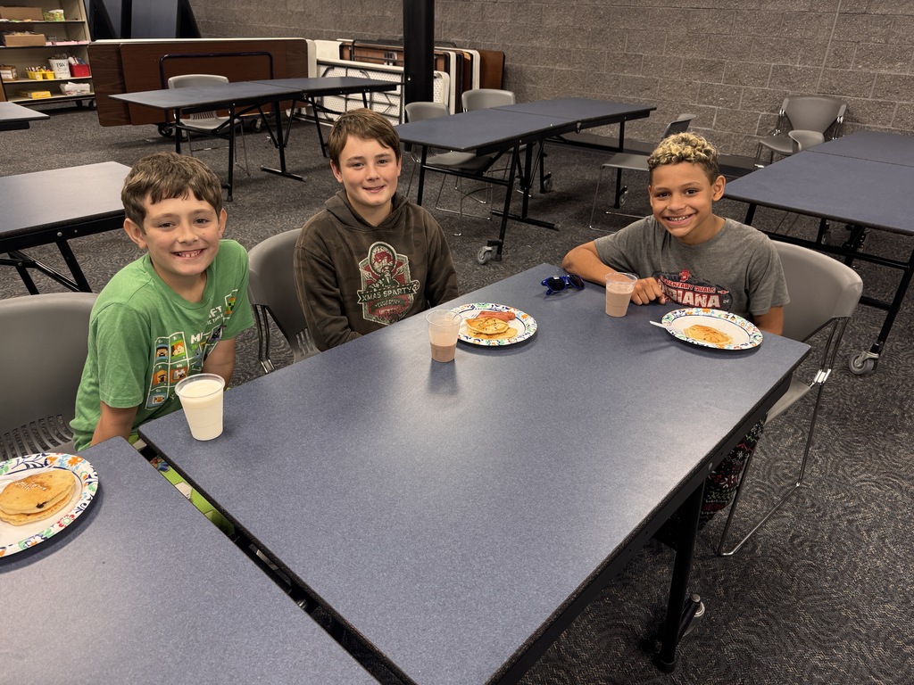3 students smile for a photo with their pancake plate in front of them. 
