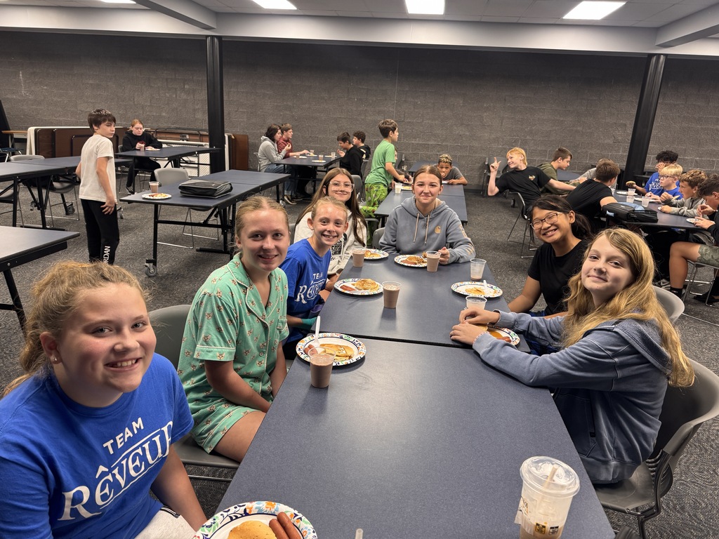 7 students smile for a photo with their pancake plate in front of them. 