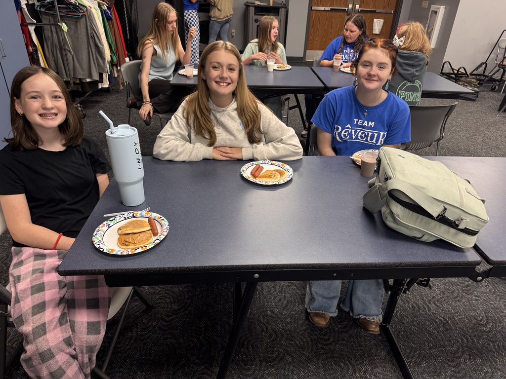 3 students smile for a photo with their pancake plate in front of them. 