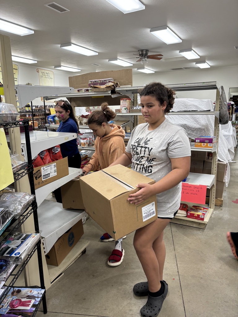 One student holding a box, another student grabbing a box off a shelf and another student working in the background.