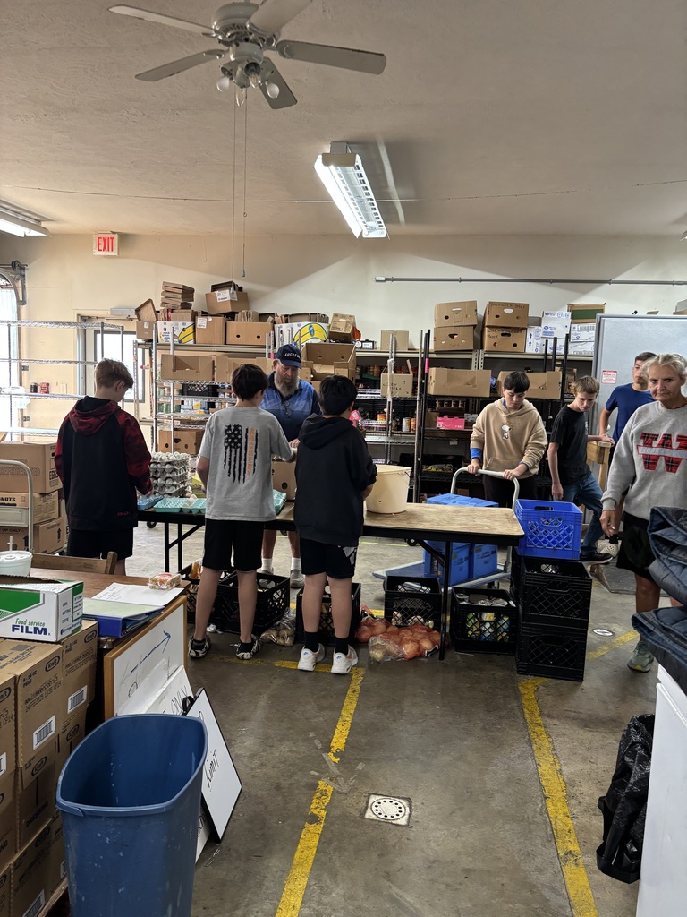 3 students packaging eggs while an adult supervises. 3 students and an adult in the background working.
