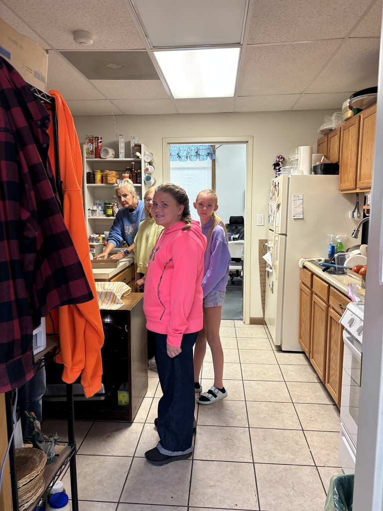 3 students standing around a counter posing for the photo while one adult shows them their next task. 